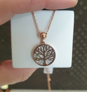 Une main qui montre un collier arbre de vie en acier rosé de la marque Lotus